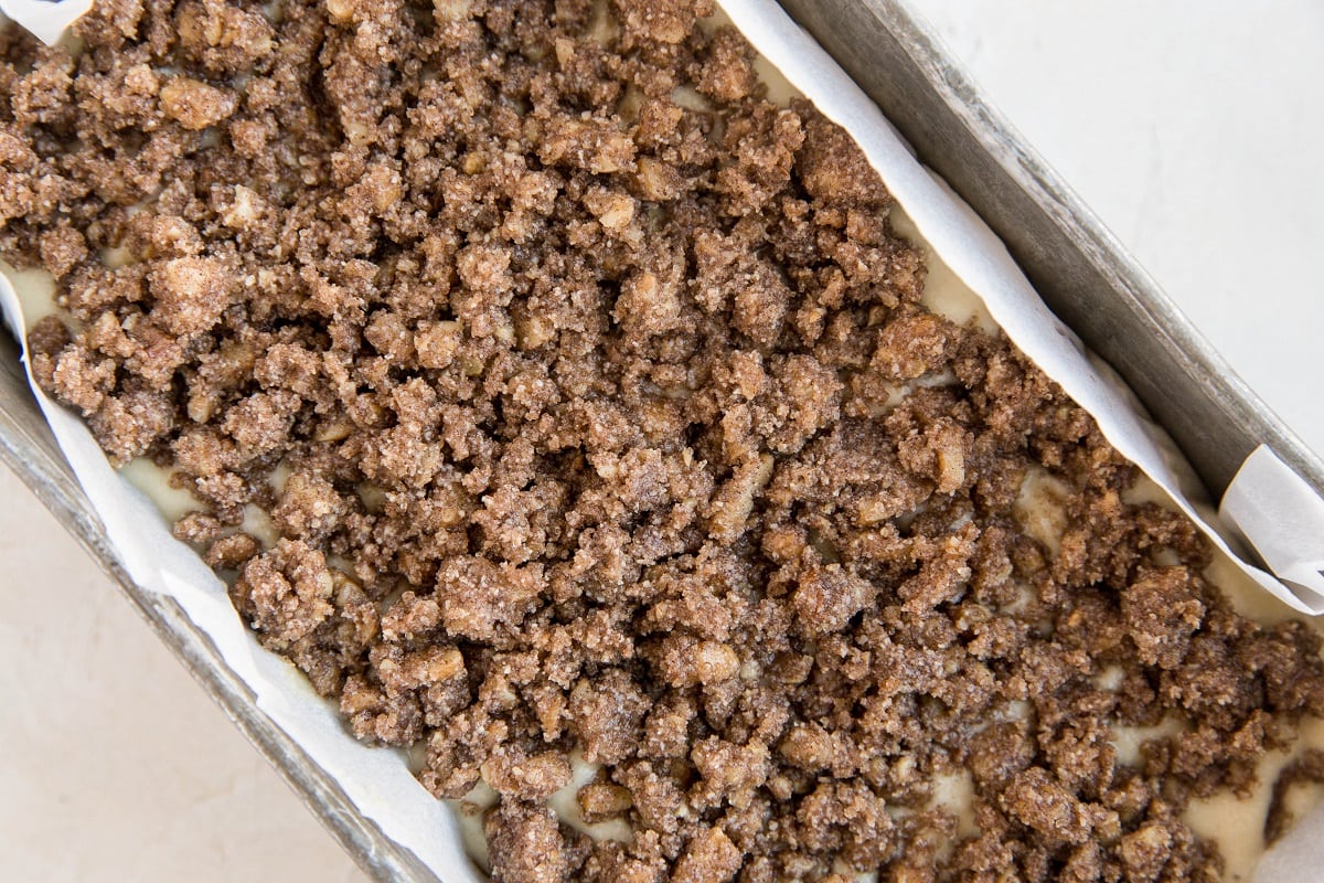 Loaf pan with banana bread batter and cinnamon streusel topping inside, ready to go into the oven to bake into banana bread.