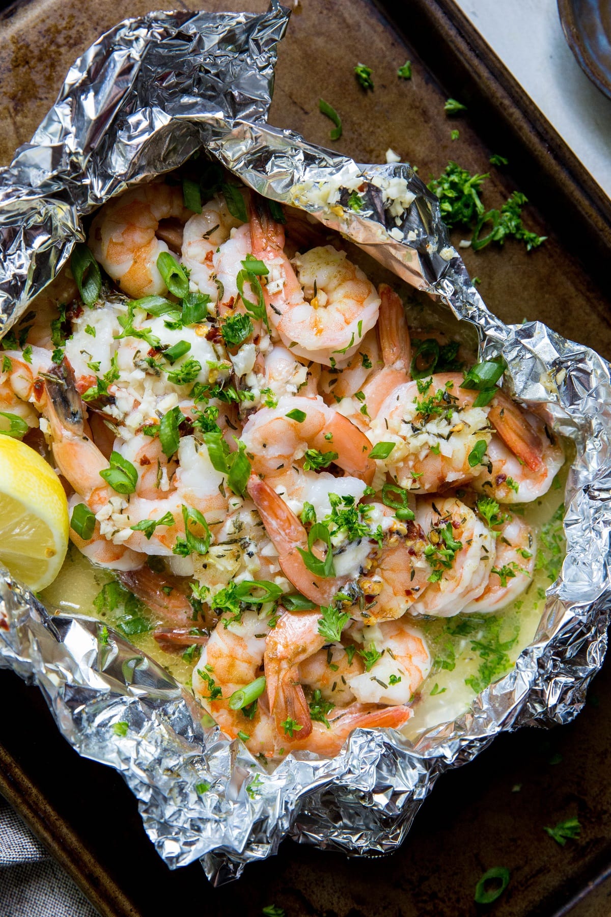 Large sheet of aluminum foil with cooked shrimp and butter, herbs, lemon juice and garlic inside. Freshly cooked.