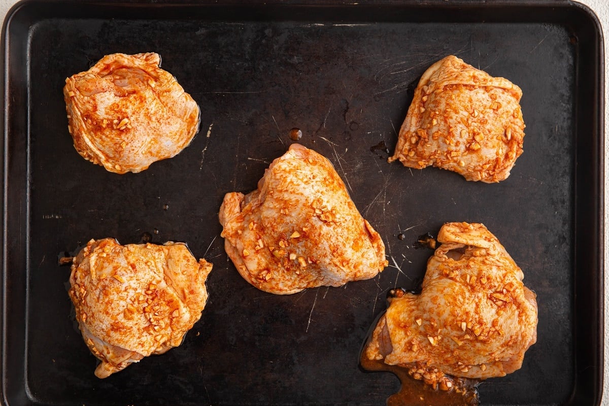 Marinated skin on chicken thighs on a baking sheet, ready to be baked.