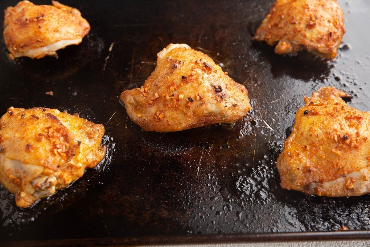 Baked chicken thighs on a cookie sheet, fresh out of the oven.