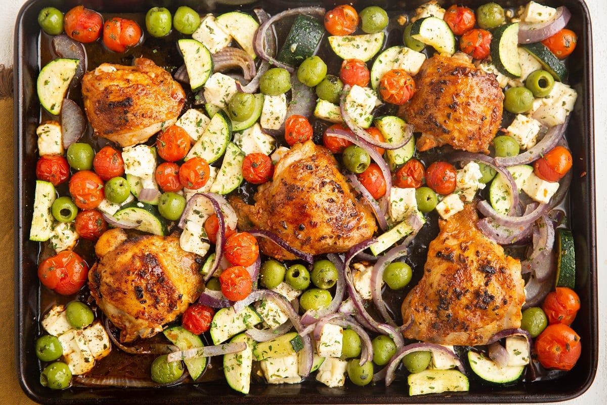Finished Mediterranean chicken and vegetables on a sheet pan, fresh out of the oven.