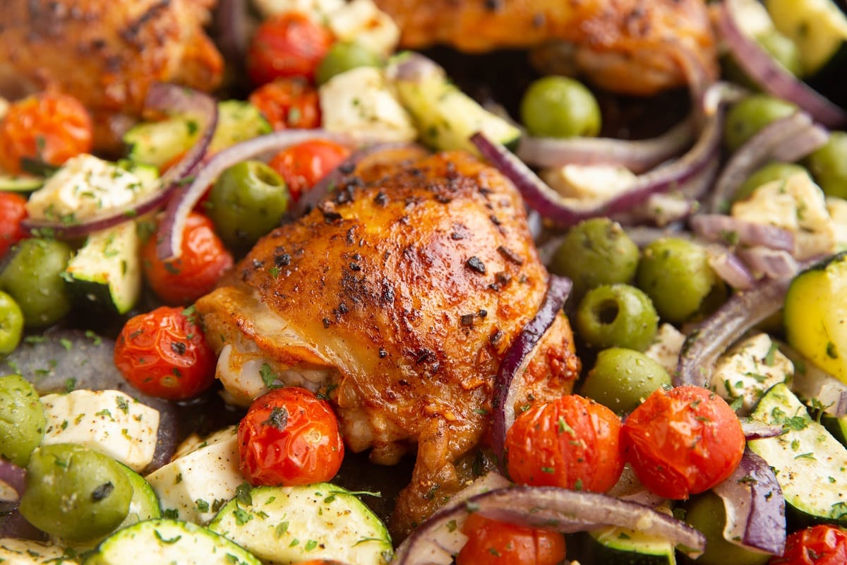 Close up image of crispy skin on chicken thigh with fresh vegetables all around it.