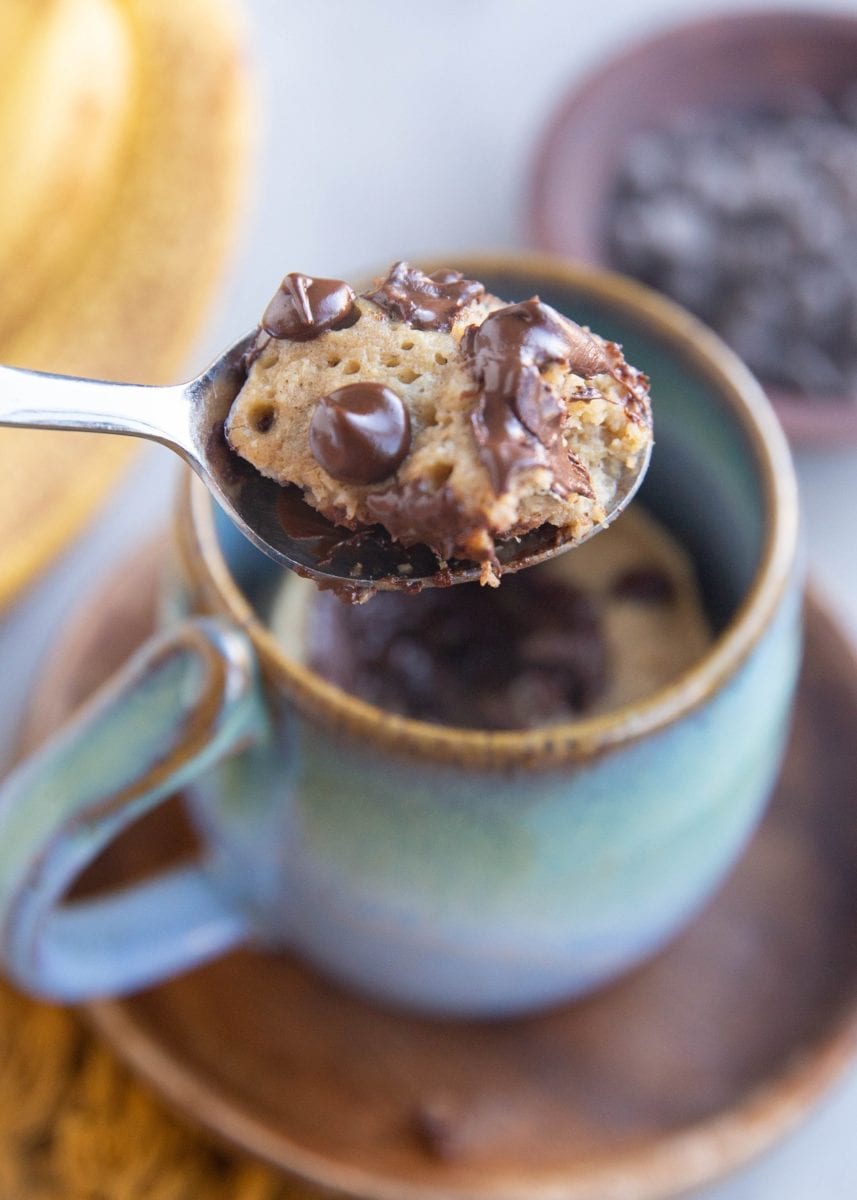 Spoon with a spoonful of banana bread mug cake with chocolate chips, ready to take a bite.