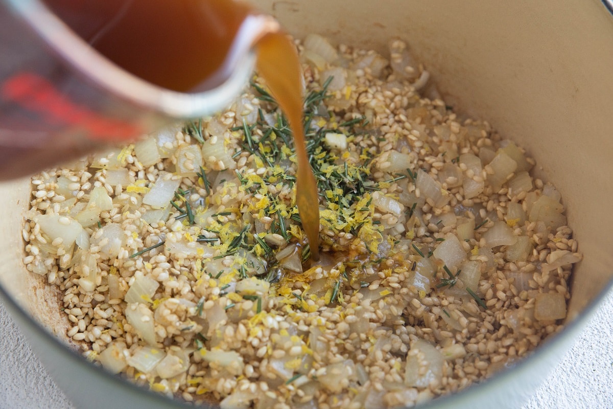 Pouring broth into a pot with rice, onion, and seasonings