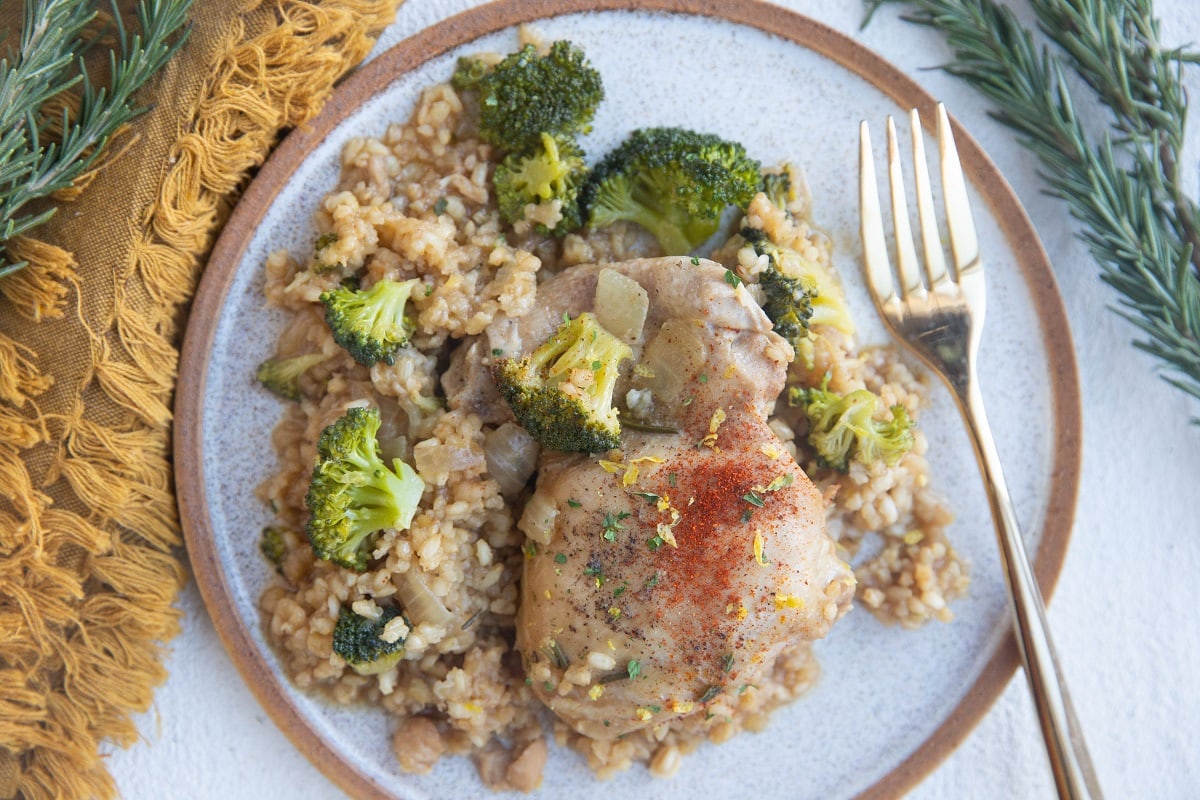 Plate with a boneless skinless chicken thigh, brown rice, and broccoli with a gold fork.