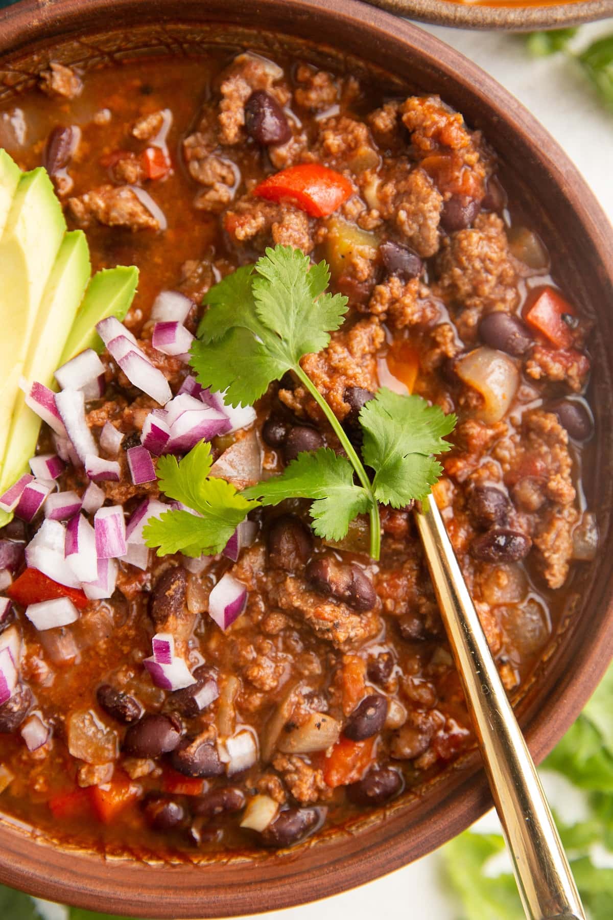 Close up on a bowl of beef chili with chopped red onions and cilantro.