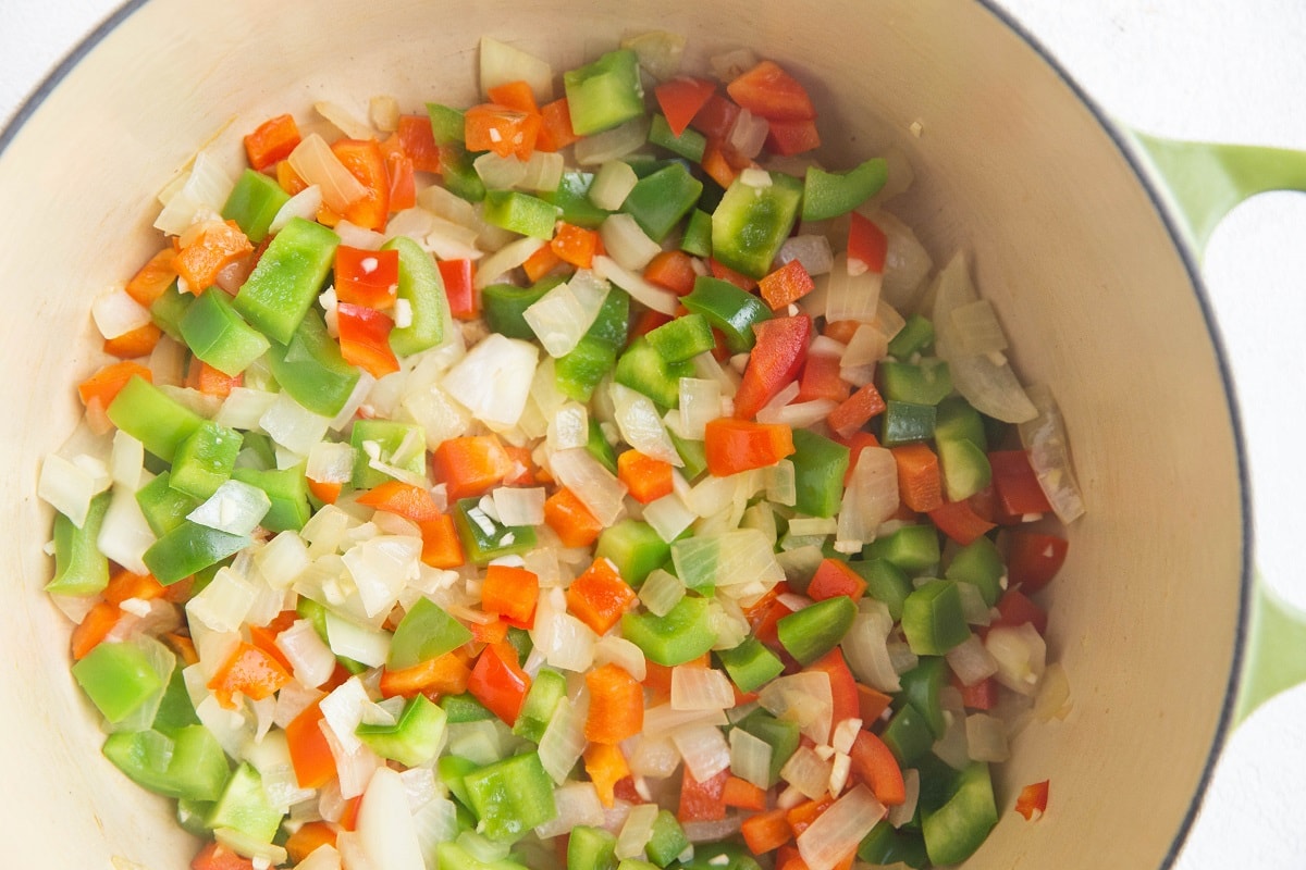 Onions and bell peppers cooking in a large pot.