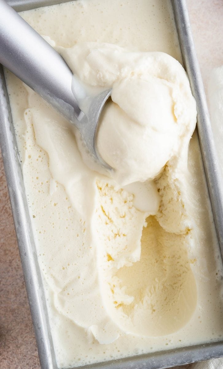 Loaf pan with homemade vanilla ice cream inside and an ice cream scooper scooping out a scoop.