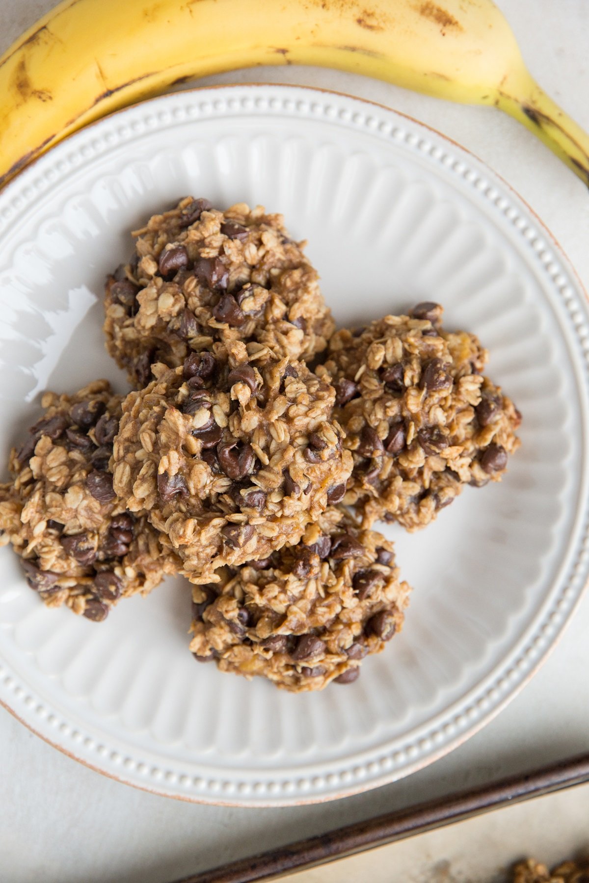 3-Ingredient Banana Oatmeal Cookies on a white plate with a ripe banana to the side.