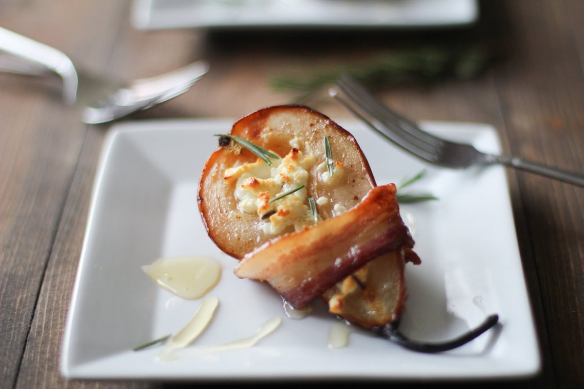Bacon Wrapped Roasted Pears with Goat Cheese and Honey on a white appetizer plate.