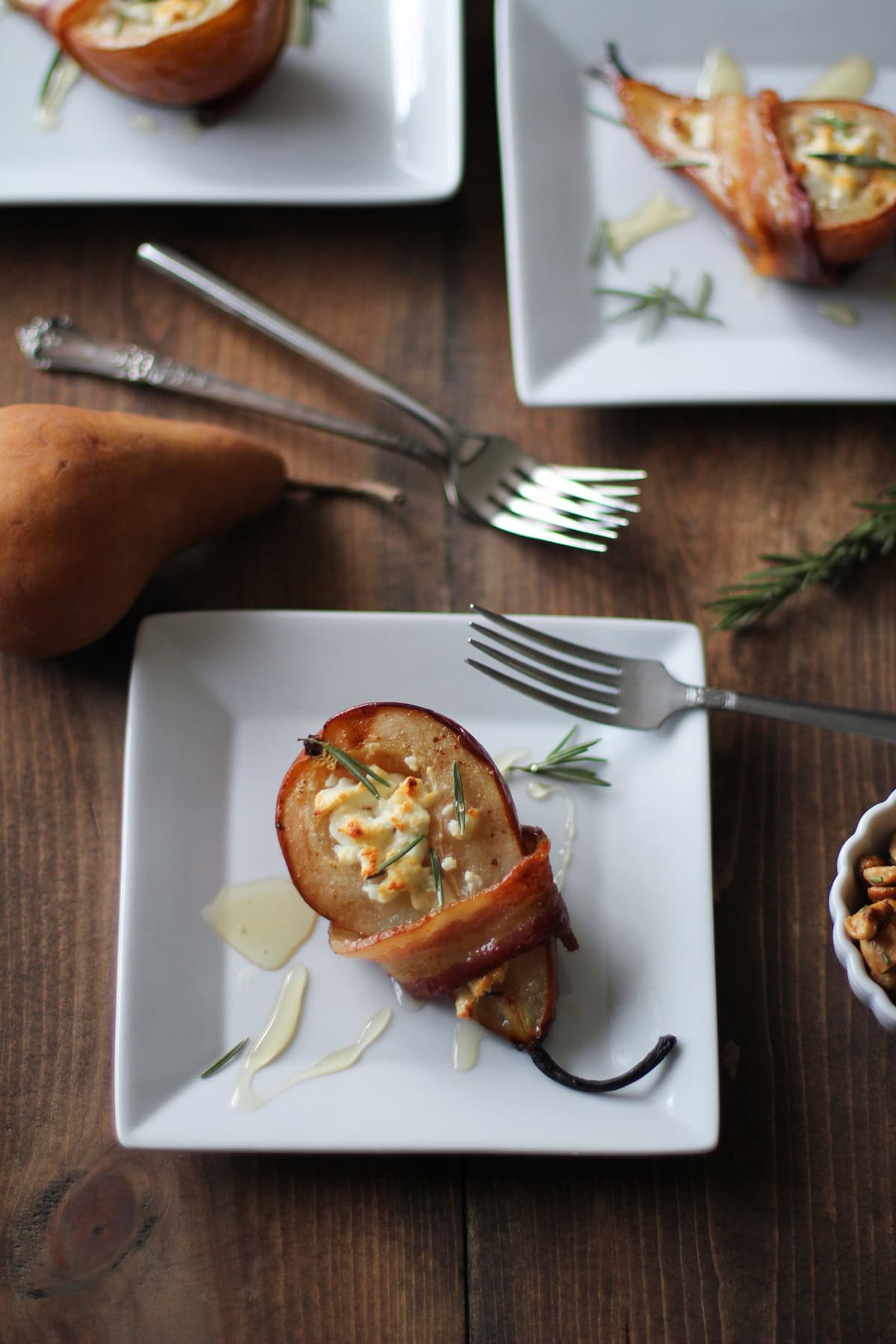 White appetizer plates with bacon wrapped pears that are stuffed with goat cheese and drizzled with honey.