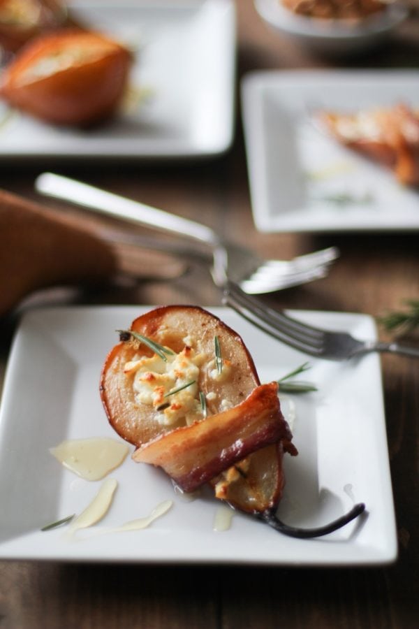 Bacon Wrapped Roasted Pears with Goat Cheese and Honey on a white appetizer plate with a fork, ready to serve.