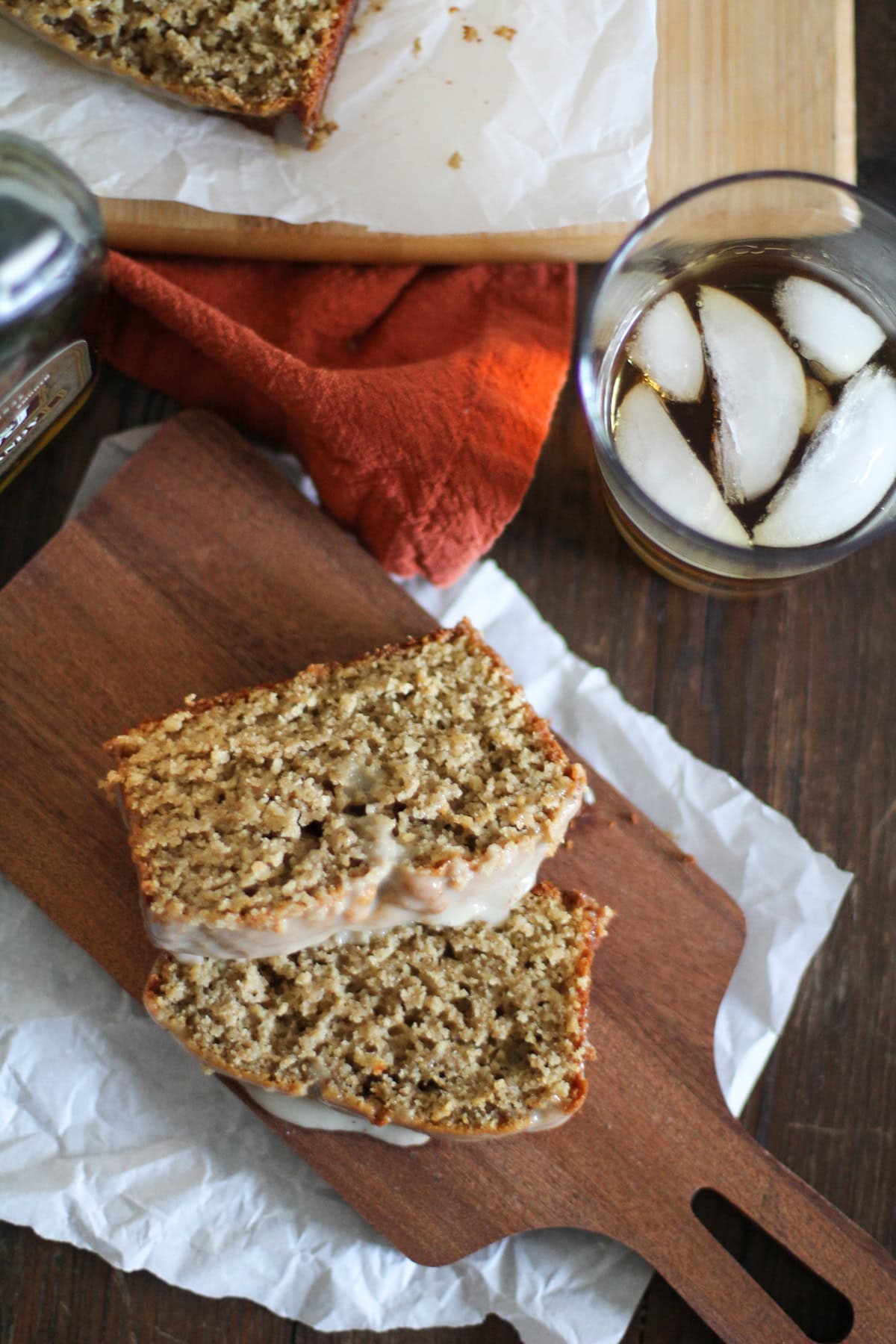 Two slices of eggnog bread on a cutting board and a glass of bourbon.