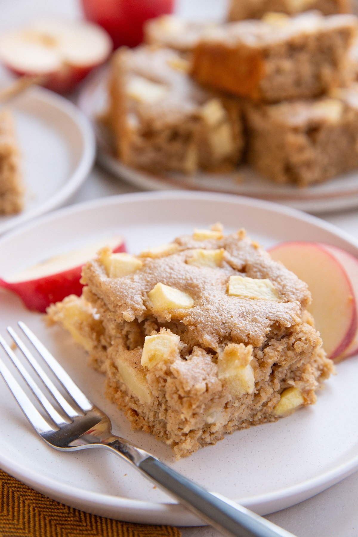 Thick slice of apple breakfast cake on a place with a plate of cake slices in the background.