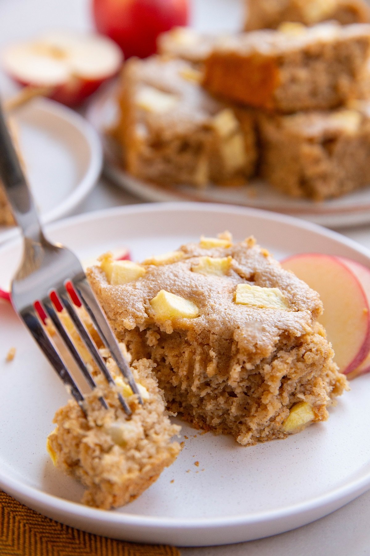 Slice of apple cake on a plate with a fork taking a bite out of it.