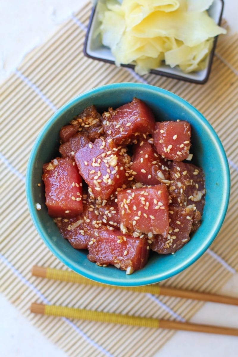 Ahi tuna poke in a teal colored bowl with chopsticks to the side and a bowl of pickled ginger. Ready to consume as an appetizer or as a main dish.