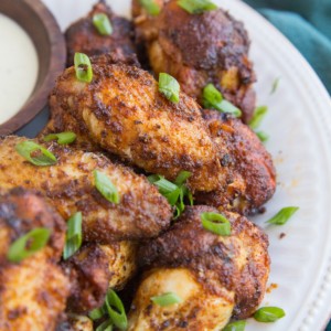 Big white plate with a pile of dry rub air fried chicken wings sprinkled with green onions with a dark blue napkin to the side.