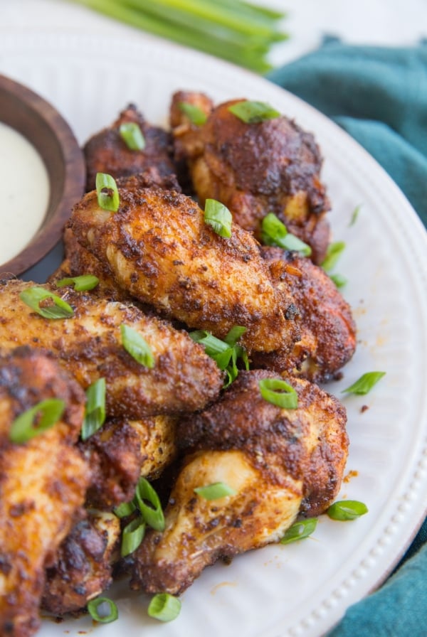 Big white plate with a pile of dry rub air fried chicken wings sprinkled with green onions with a dark blue napkin to the side.