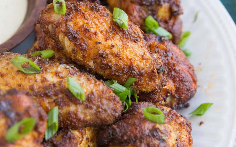 Big white plate with a pile of dry rub air fried chicken wings sprinkled with green onions with a dark blue napkin to the side.