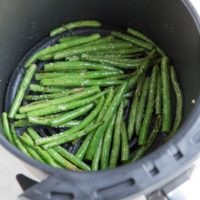 Air fryer green beans inside of the basket of an air fryer, ready to serve with a main dish.
