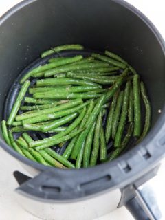 Air fryer green beans inside of the basket of an air fryer, ready to serve with a main dish.