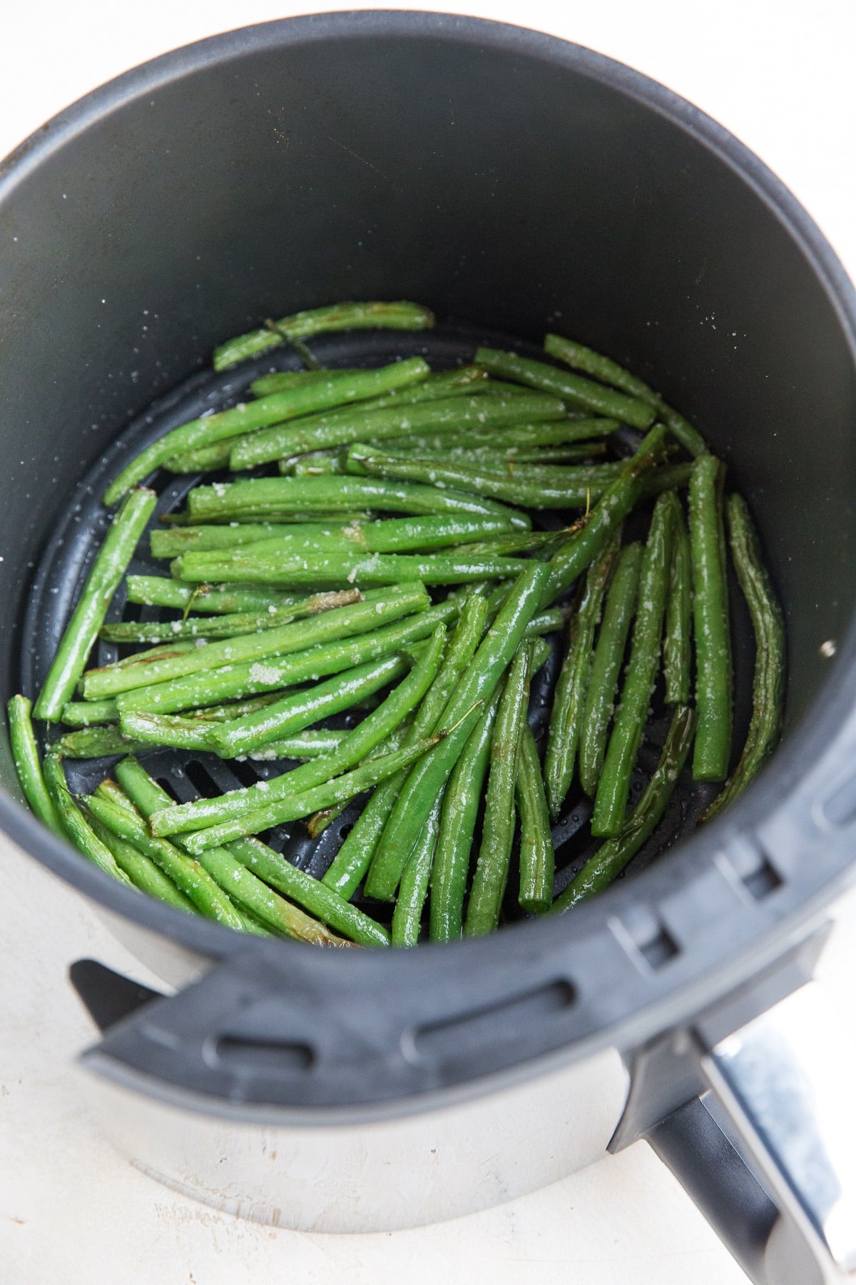 Air fryer green beans inside of the basket of an air fryer, ready to serve with a main dish.