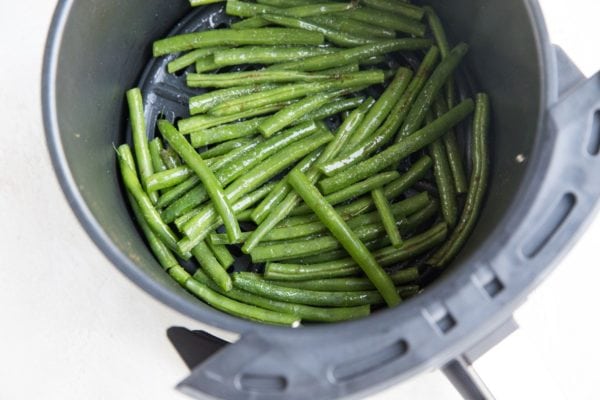 raw green beans coated in oil and salt in an air fryer.