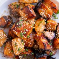 Finished air fryer salmon bites on a white plate, sprinkled with sesame seeds and fresh herbs.