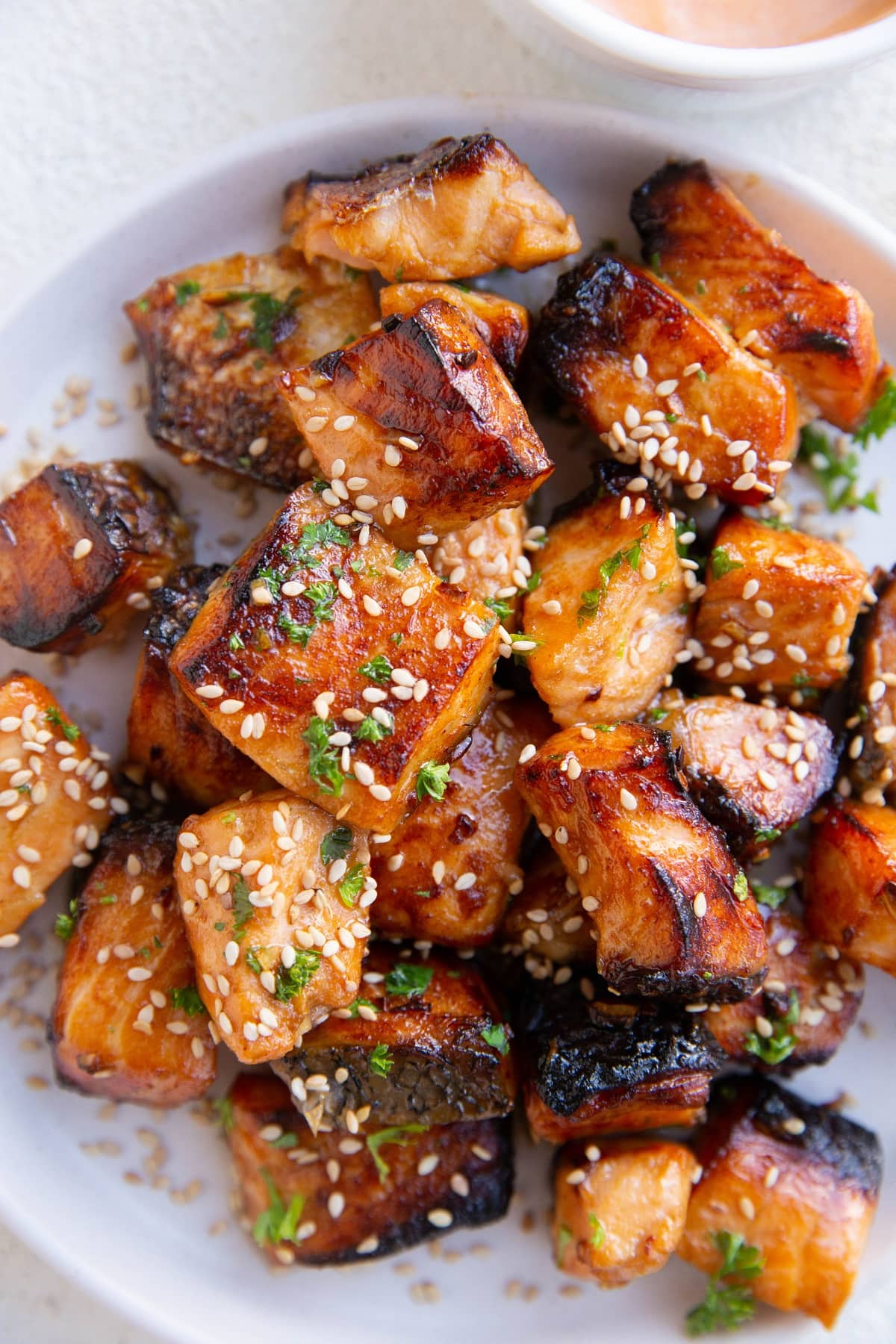 Finished air fryer salmon bites on a white plate, sprinkled with sesame seeds and fresh herbs.