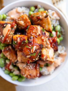 Air fryer salmon bites in a white bowl on top of steamed brown rice and edamame. A gold fork and napkin to the side.