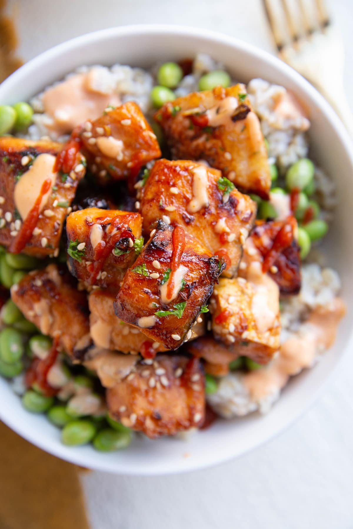 Air fryer salmon bites in a white bowl on top of steamed brown rice and edamame. A gold fork and napkin to the side.