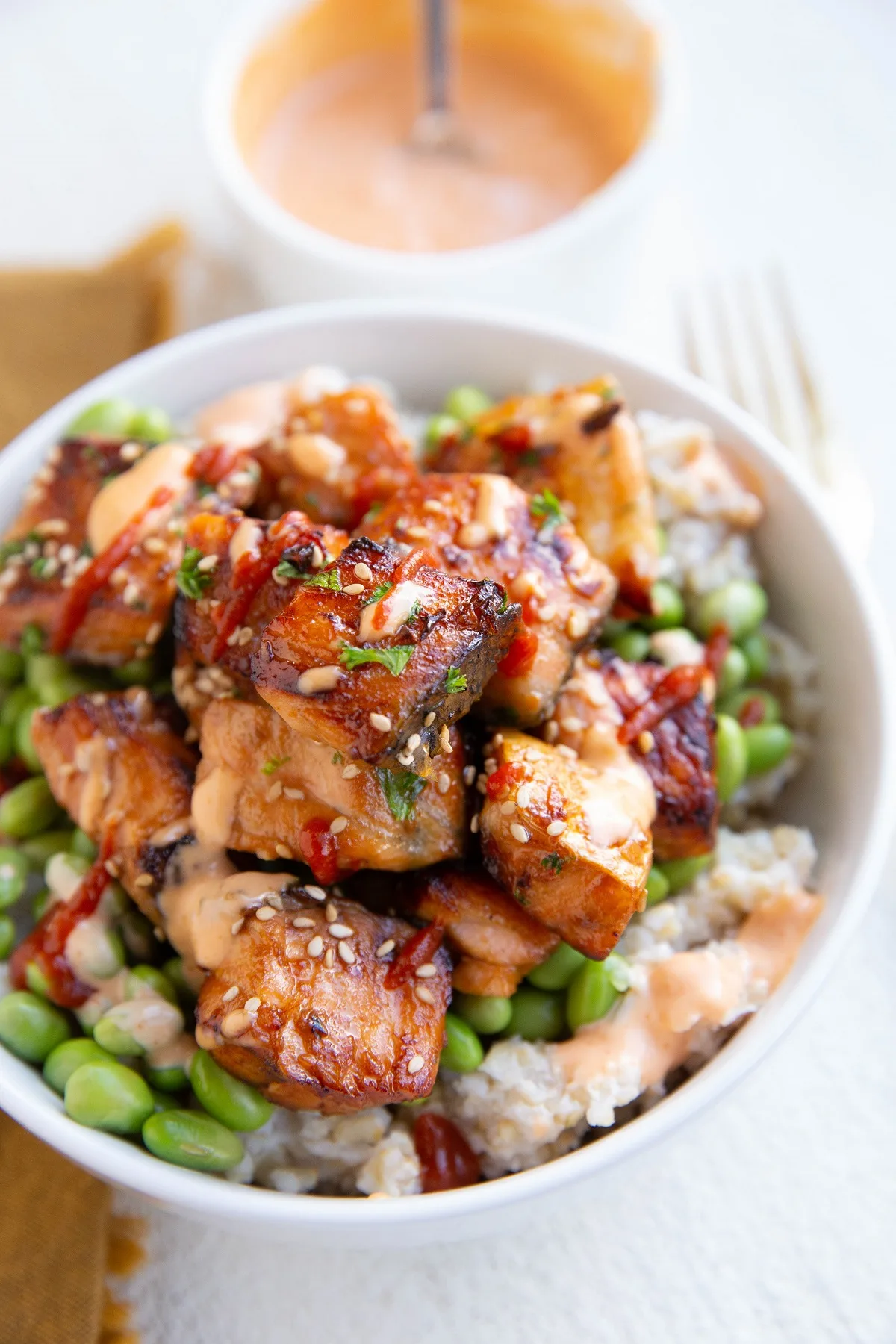 Air fryer salmon bites in a bowl with edamame, brown rice, sriracha and spicy mayo sauce. A complete meal, ready to eat.