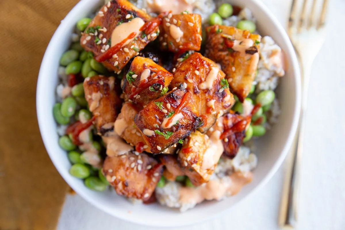 Air fryer salmon bites in a bowl with spicy mayo sauce, edamame, and brown rice.