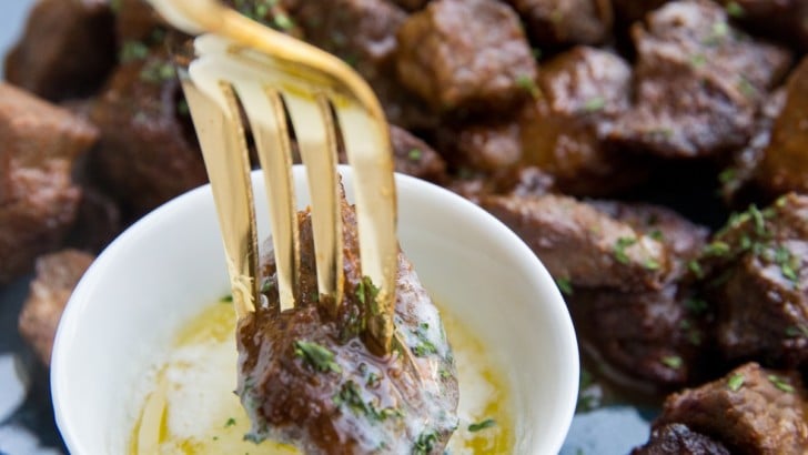 Blue plate full of air fryer steak bites with a small bowl of melted butter and a fork dipping a steak bite into the butter.