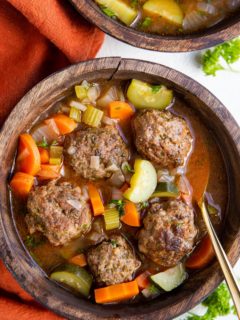 Two bowls of Albondigas soup in wooden bowls with a red napkin to the side and fresh parsley