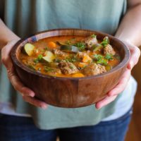 Woman holding a big wooden bowl of Mexican Meatball Soup