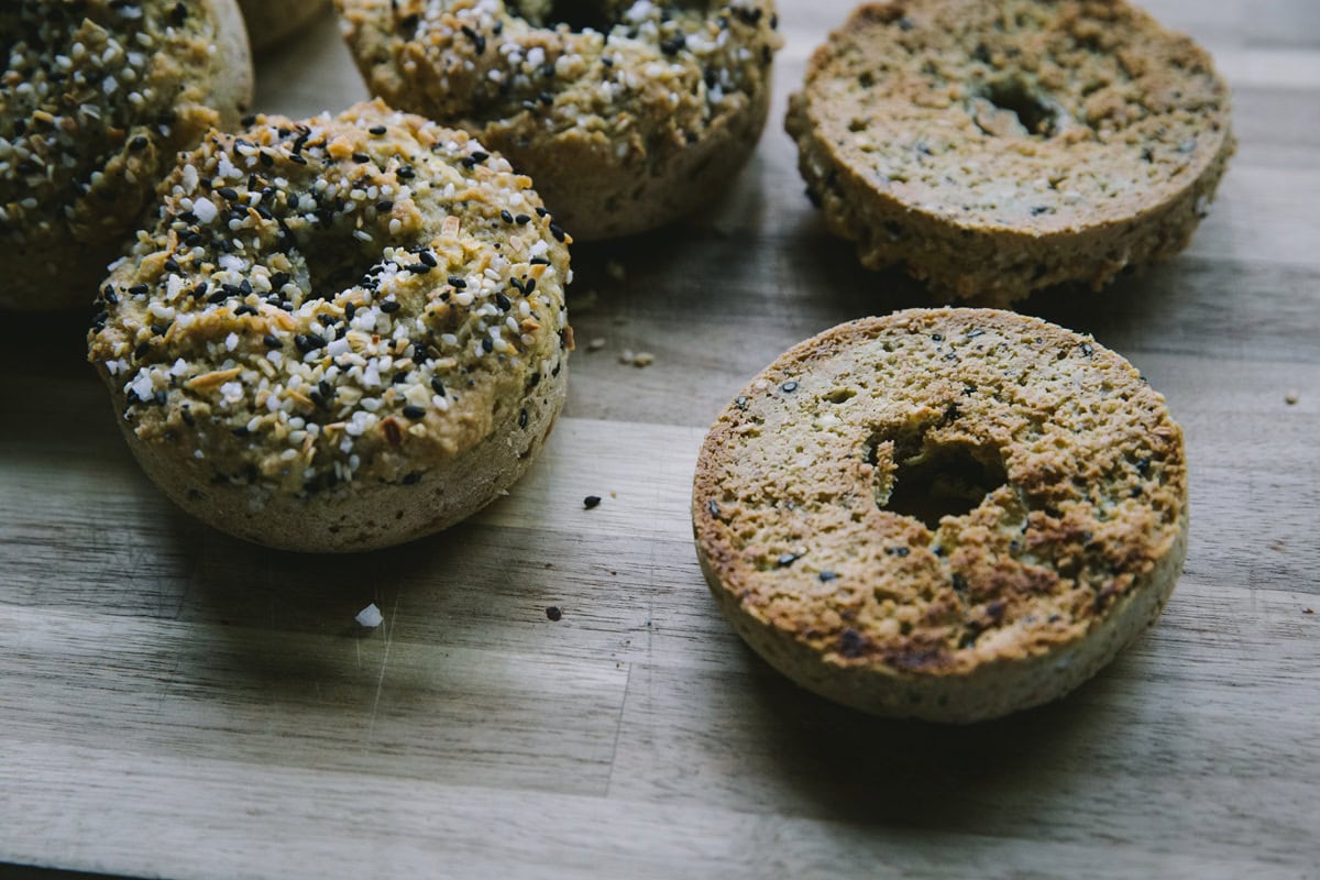 Cutting board with homemade everything bagels on top, one sliced in half and toasted.