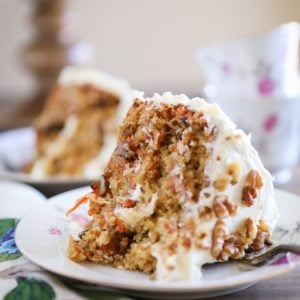 Thick slice of carrot cake on a decorative plate with a flowered napkin to the side.