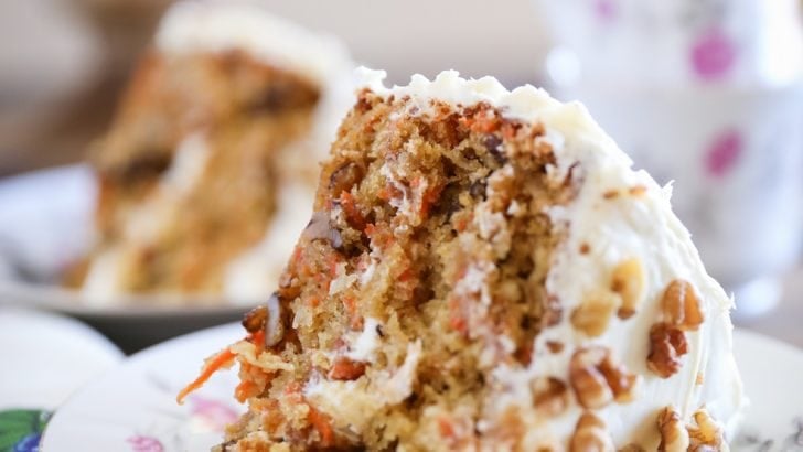 Thick slice of carrot cake on a decorative plate with a flowered napkin to the side.