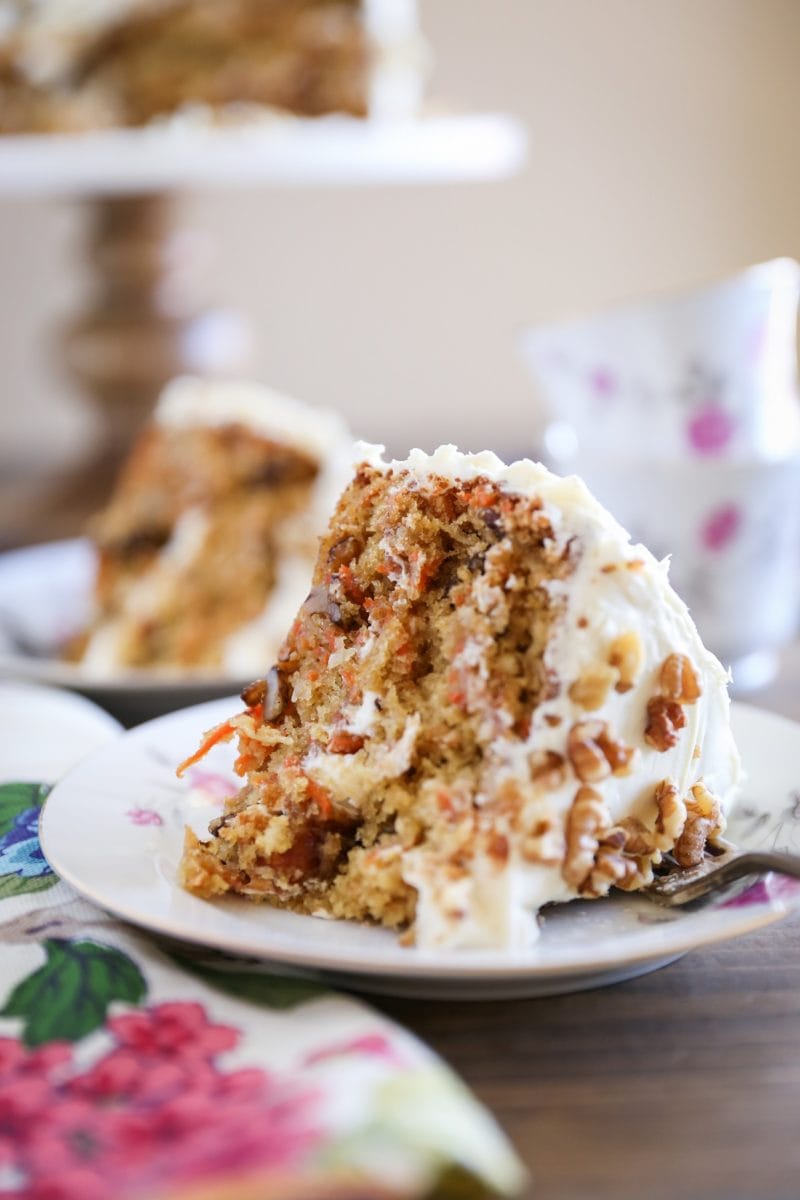 Thick slice of carrot cake on a decorative plate with a flowered napkin to the side.
