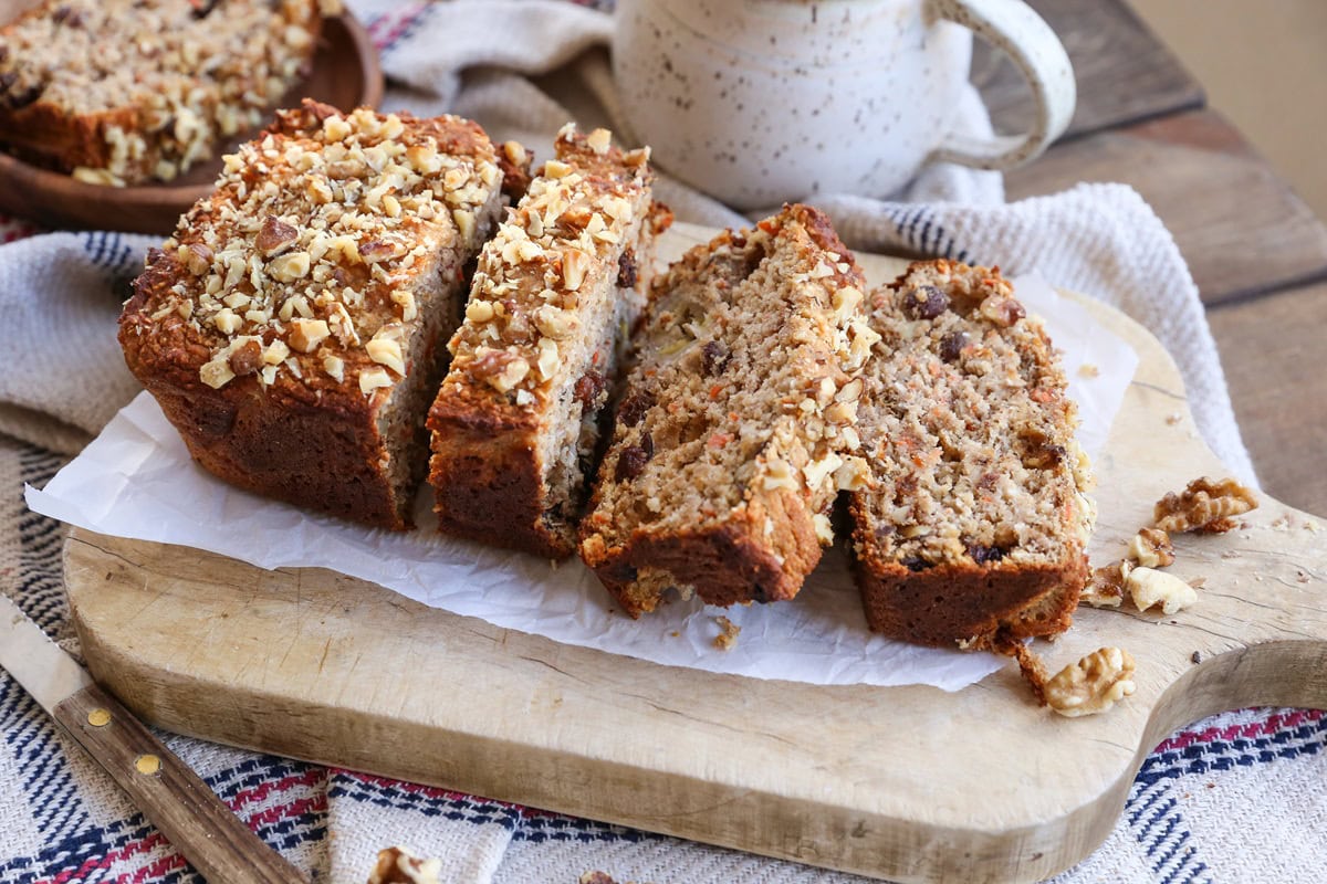 Loaf of carrot banana bread on top of a wooden cutting board, cut into slices.