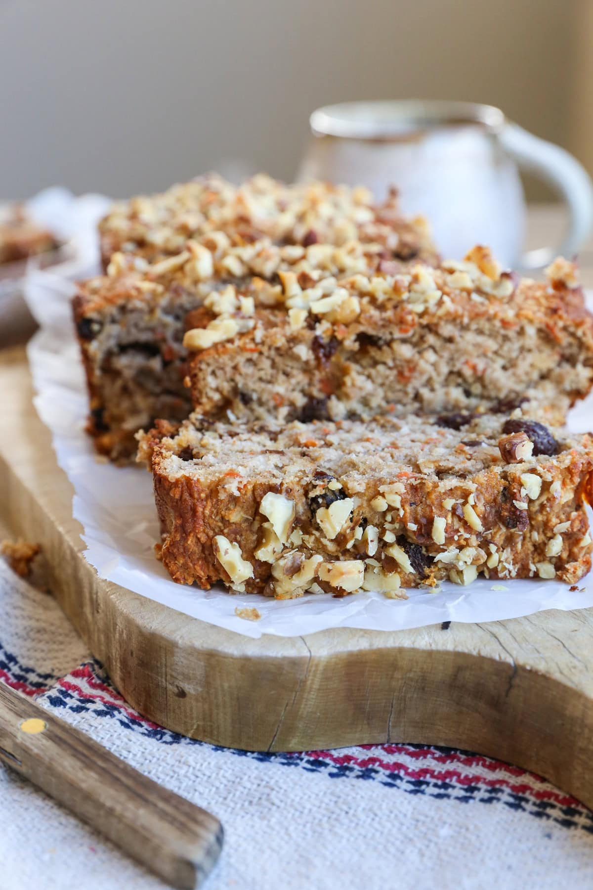 Carrot cake loaf on a wooden cutting board cut into slices with a wooden handle knife to the side.