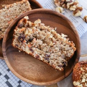 Piece of carrot cake banana bread on a wooden plate with the rest of the loaf to the side.