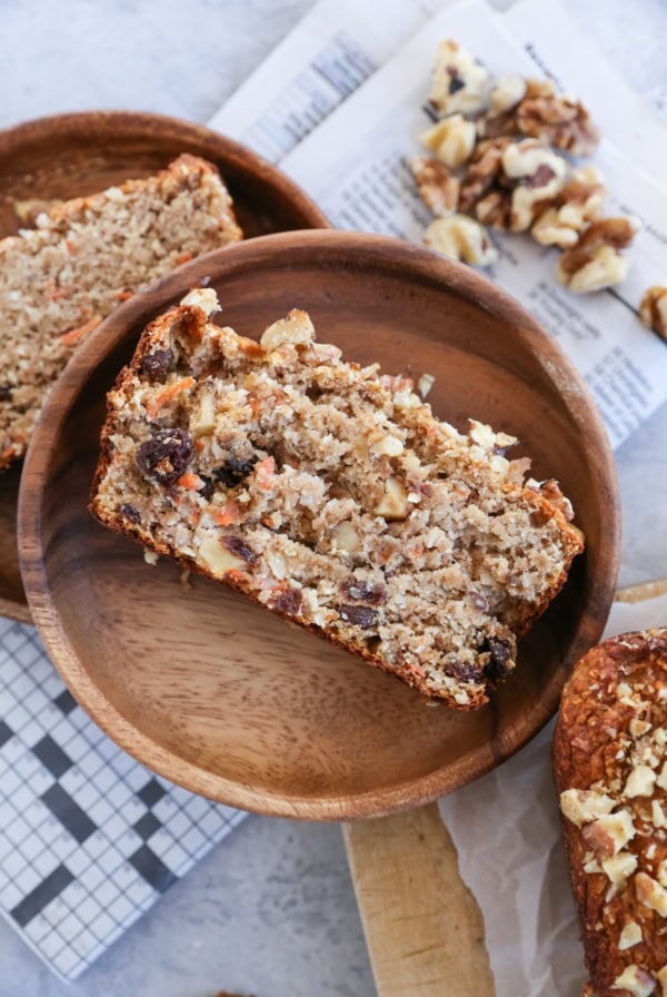 Piece of carrot cake banana bread on a wooden plate with the rest of the loaf to the side.
