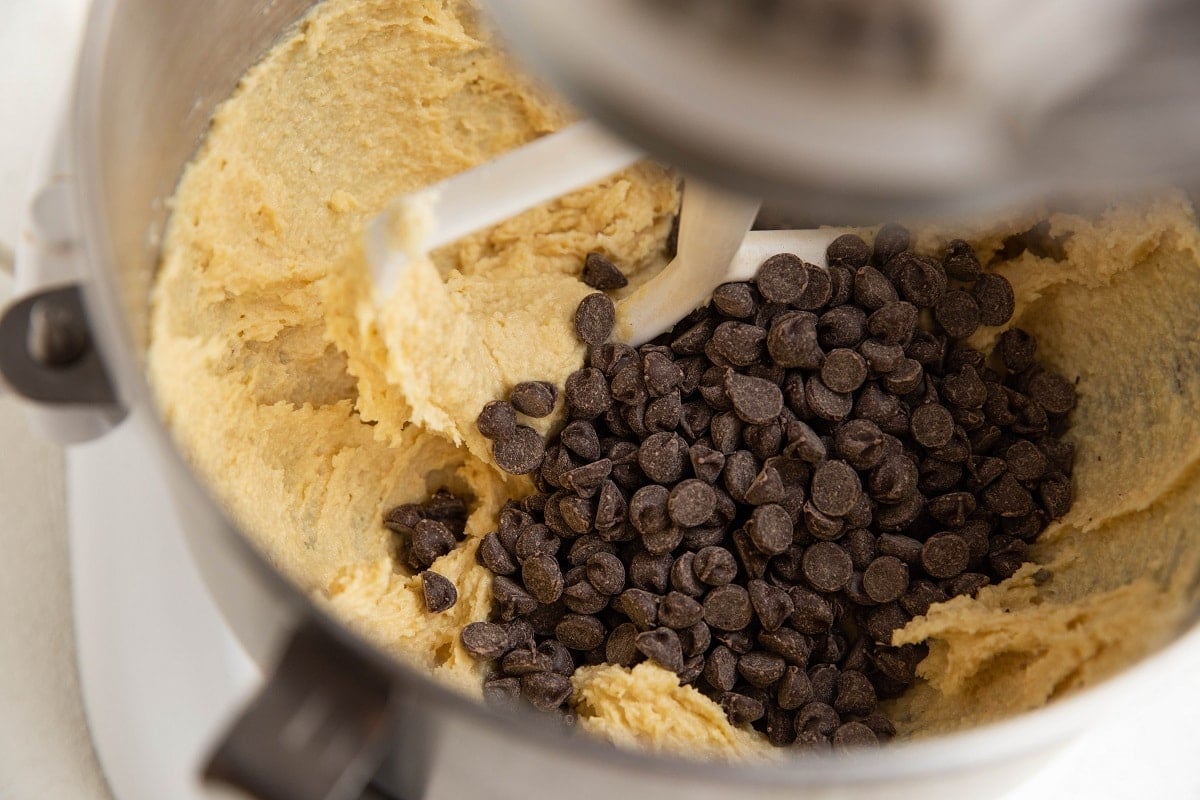 Chocolate chips on top of almond flour cookie dough in a mixer, ready to be mixed in.