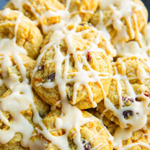 Pile of cranberry orange cookies drizzled with an orange glaze on a blue plate.