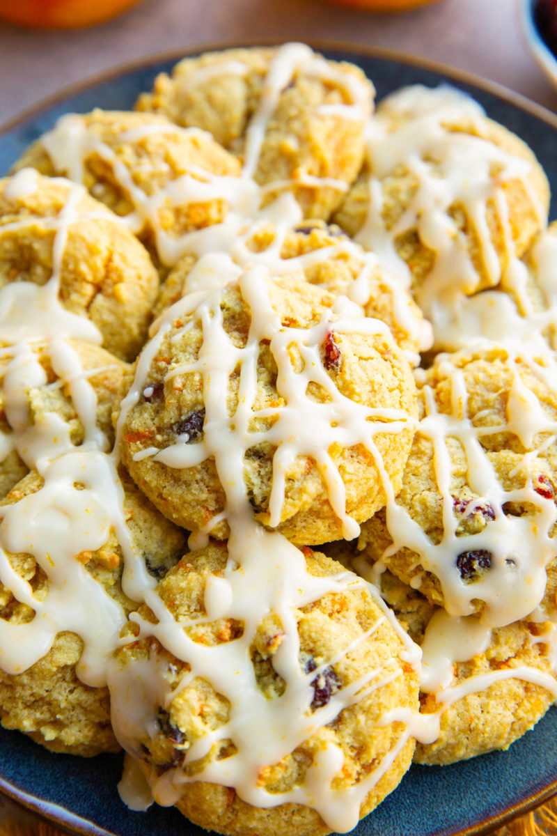 Pile of cranberry orange cookies drizzled with an orange glaze on a blue plate.