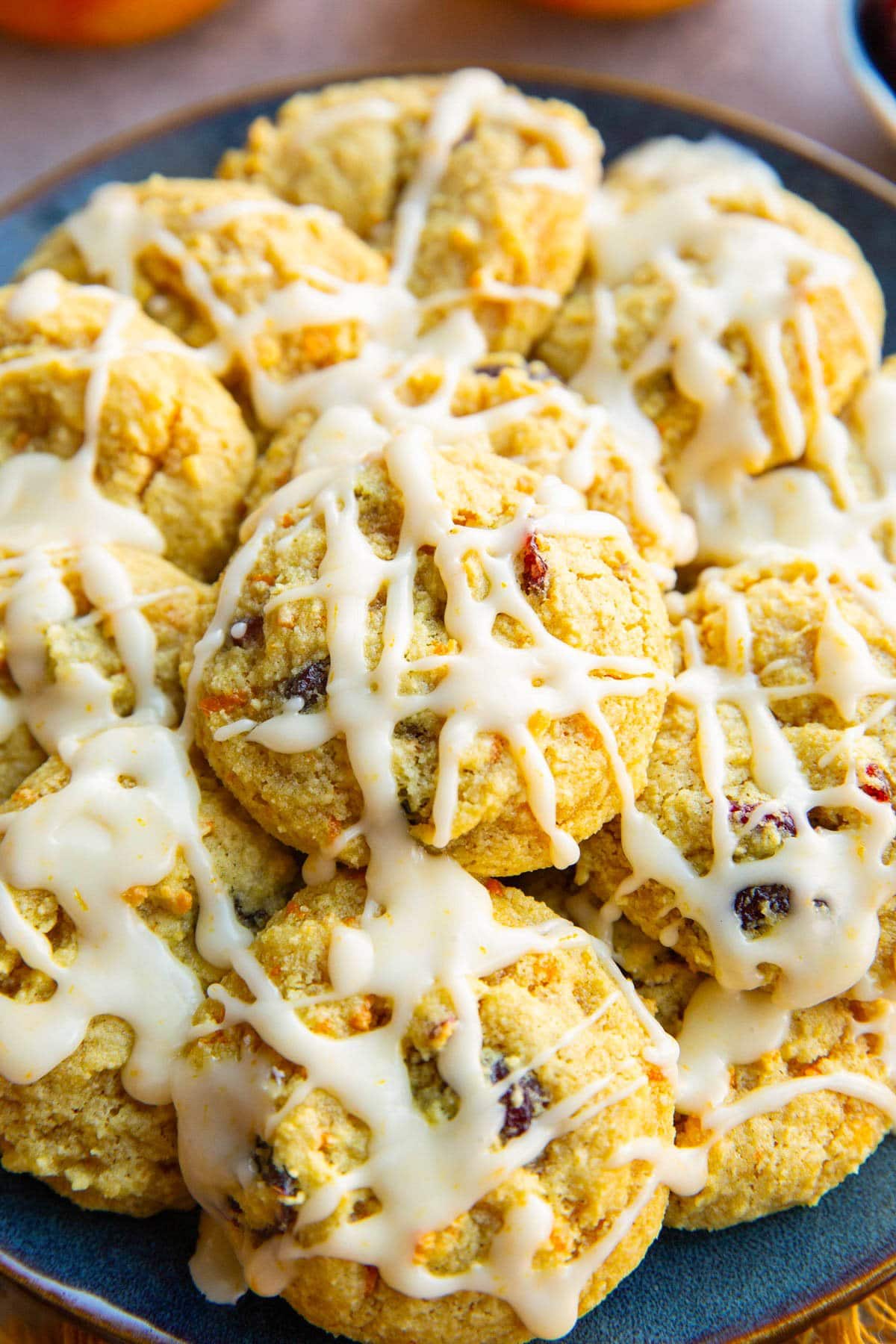Pile of cranberry orange cookies drizzled with an orange glaze on a blue plate.