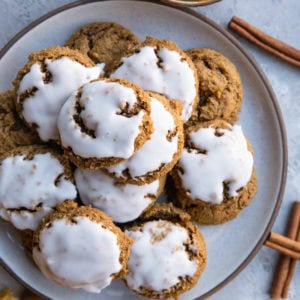 Iced ginger molasses cookies on a plate with fresh nutmeg and cinnamon sticks to the side, ready to serve.