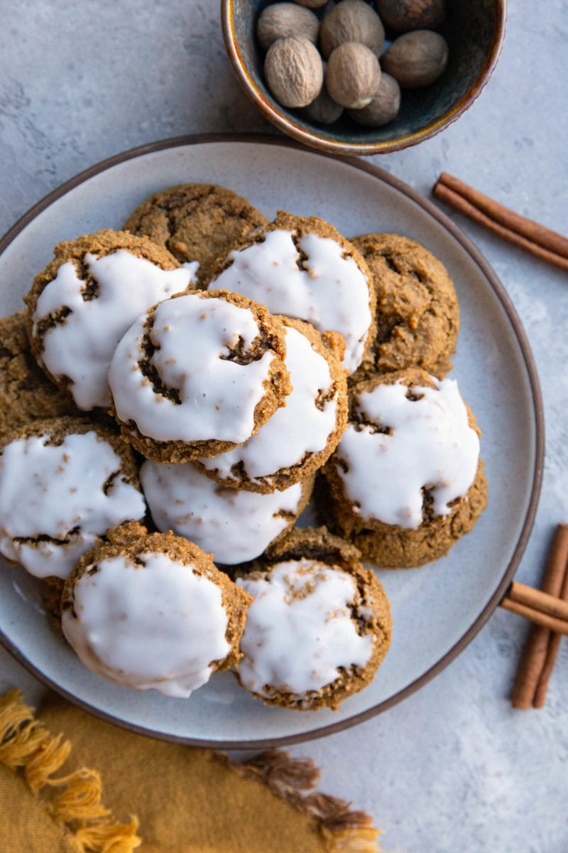 Iced ginger molasses cookies on a plate with fresh nutmeg and cinnamon sticks to the side, ready to serve.